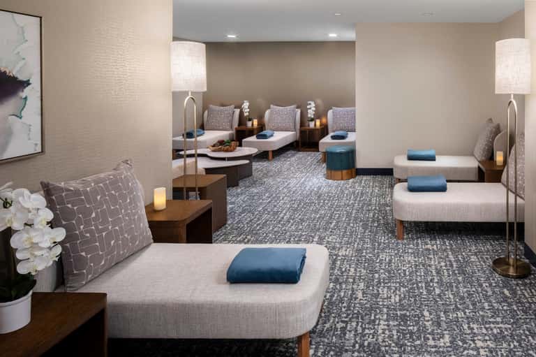 Spa relaxation room with multiple lounge chairs, soft lighting, white orchid decor, and calming neutral tones