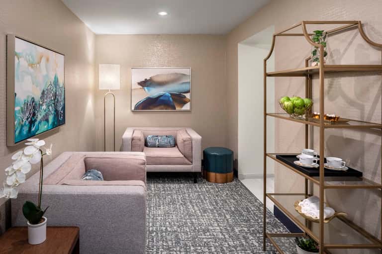 Modern hotel lounge with beige sectional sofa, abstract wall art, and metal shelving unit