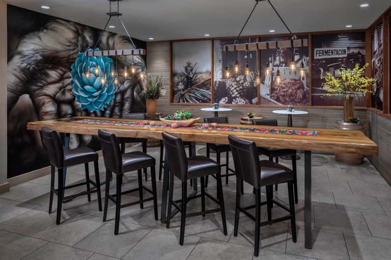 Modern bar with long wooden counter, bar seating, and artistic wall murals
