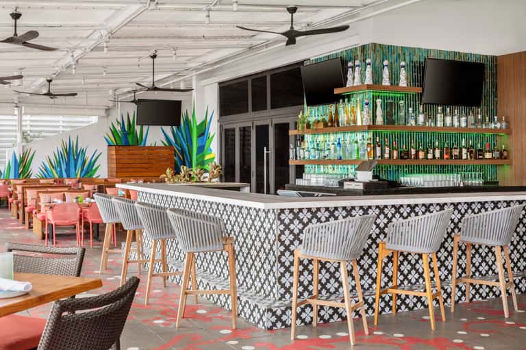 Stylish rooftop bar with geometric patterned counter, potted plants, glass shelving, and modern seating