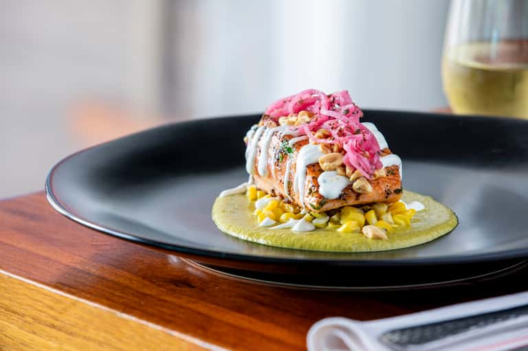 Gourmet plated dish with pink garnish and yellow corn on black plate
