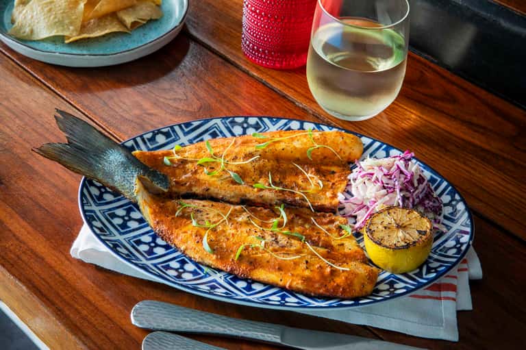 Grilled fish dish with purple cabbage slaw and lemon on decorative blue plate