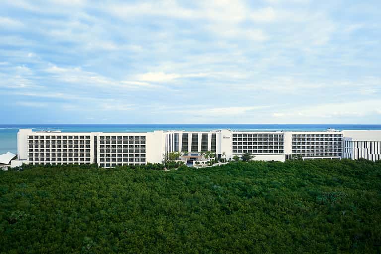 Modern Hilton hotel complex overlooking ocean with white buildings and surrounding tropical forest