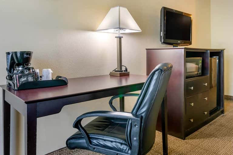 Hotel room work desk with lamp, television, coffee maker, and dark wood furniture