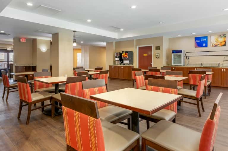 Hotel dining area with wooden tables, red striped chairs, wood accents, and recessed ceiling lights