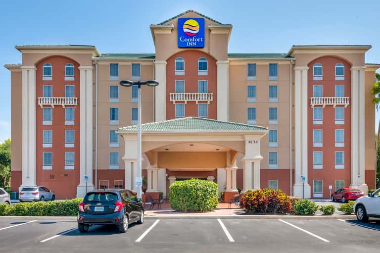 Comfort Inn hotel exterior with red and tan facade, white columns, green roof, parking lot entrance