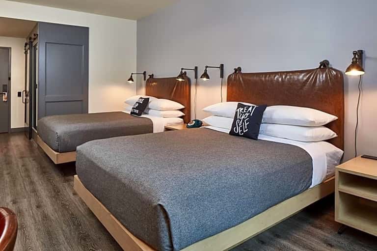 Modern hotel guest room with two queen beds, brown leather headboards, and contemporary lighting