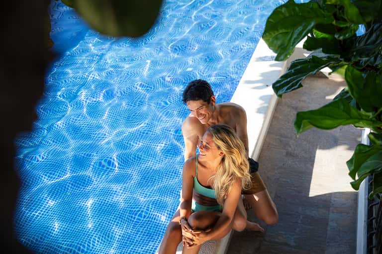 Couple enjoying resort pool with tropical plants and ocean views in background