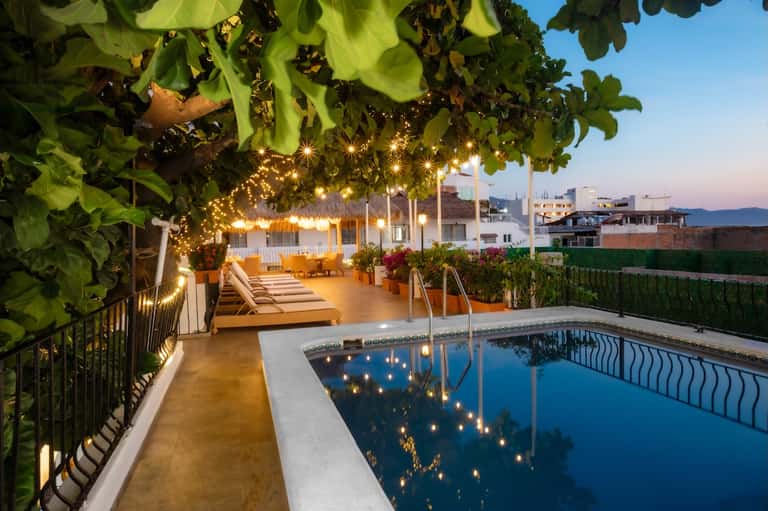 Twilight poolside patio with string lights, lounge chairs, and grapevine canopy