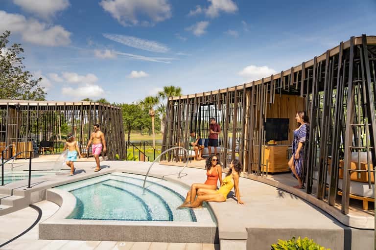 Resort pool area with hot tub, families enjoying water activities, modern wooden cabanas, palm trees, lake view