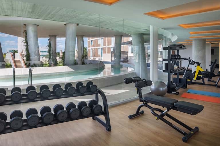 Modern fitness center with dumbbells, exercise bikes, and views of pool through glass walls