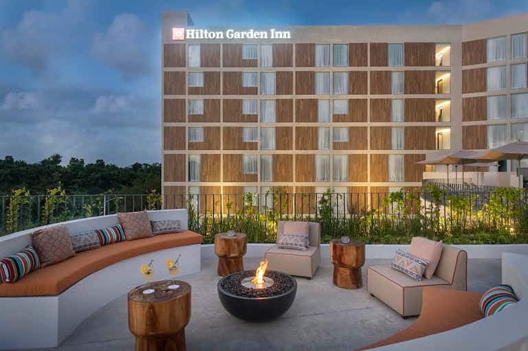 Hilton Garden Inn rooftop lounge with curved seating, fire pit, cushions, and hotel building in background at twilight