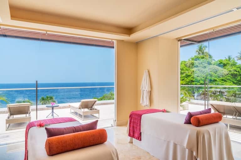 Spa treatment room with ocean views, two massage beds with colorful bolsters, and ocean-view terrace