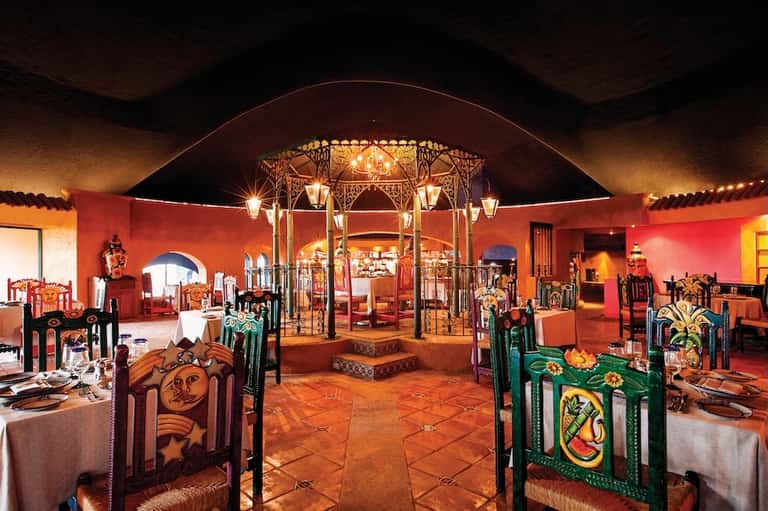 Ornate Moroccan-style dining room with red walls, decorative chairs, and central brass chandelier