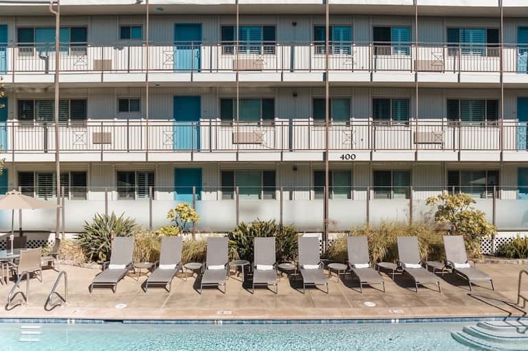 Multi-story beachfront resort building with white railings, pool, and lounge chairs below