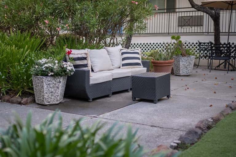 Dark wicker outdoor sofa with cushions and striped pillows surrounded by potted flowers