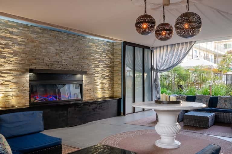Luxury outdoor lounge with fireplace, modern furniture, hanging pendant lights, and draped curtains