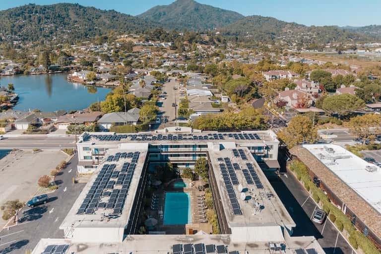 Aerial view of luxury resort with pool, solar panels, and lake surrounded by mountains