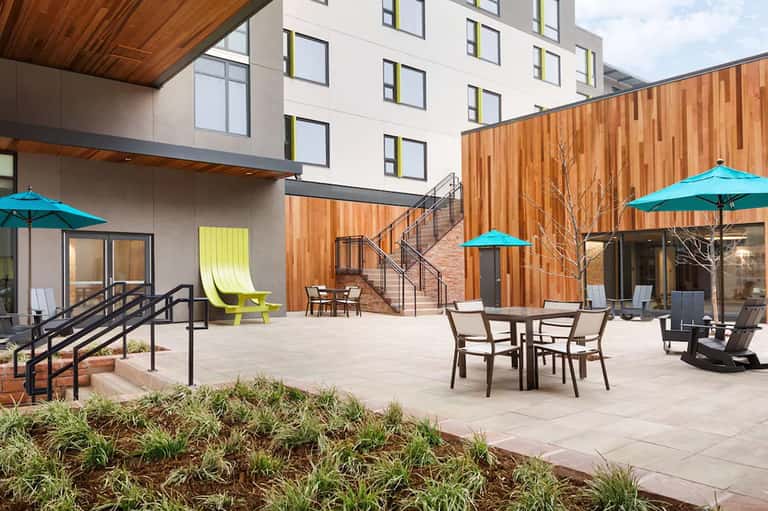 Modern hotel courtyard with wood cladding, turquoise umbrellas, dining tables, stairs, and contemporary architecture