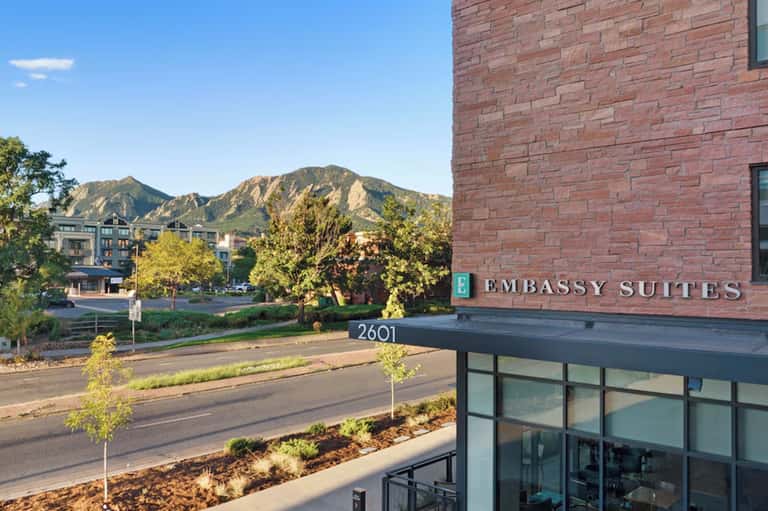Embassy Suites hotel exterior with brick facade, mountain backdrop, and street address signage