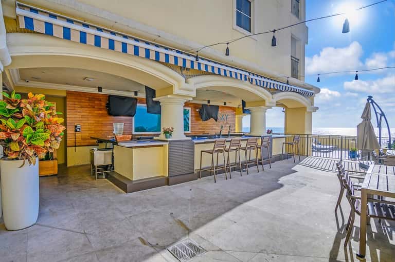 Rooftop bar and lounge with blue striped awning, yellow walls, ocean views, and casual seating