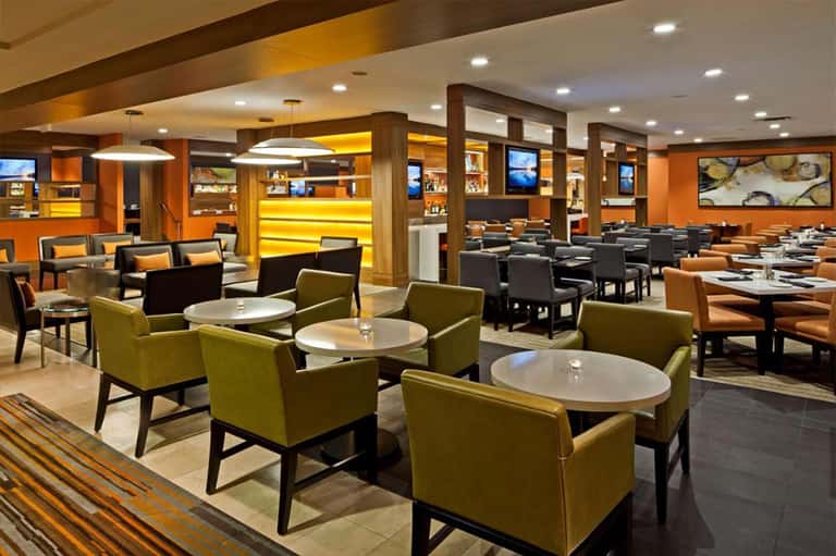 Contemporary restaurant interior with olive seating, orange accent walls, and modern pendant lighting