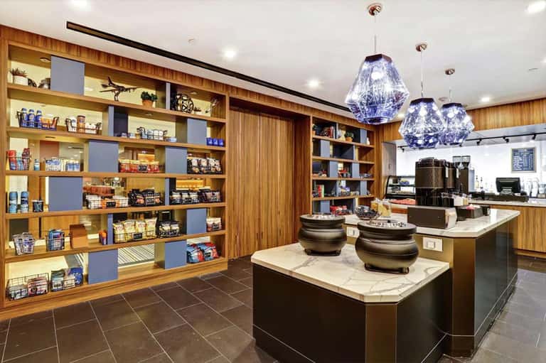 Modern resort café with wooden shelving displaying merchandise, pendant lighting, and service counter