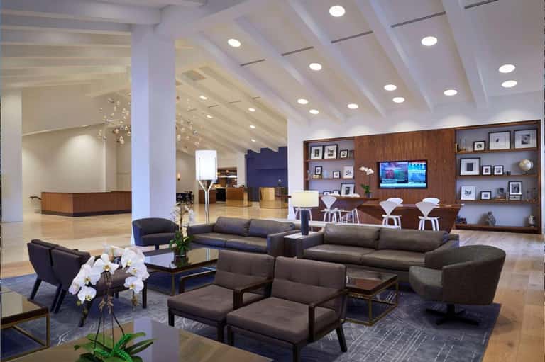Modern hotel lobby featuring dark sofas, wood accents, marble flooring, and reception desk