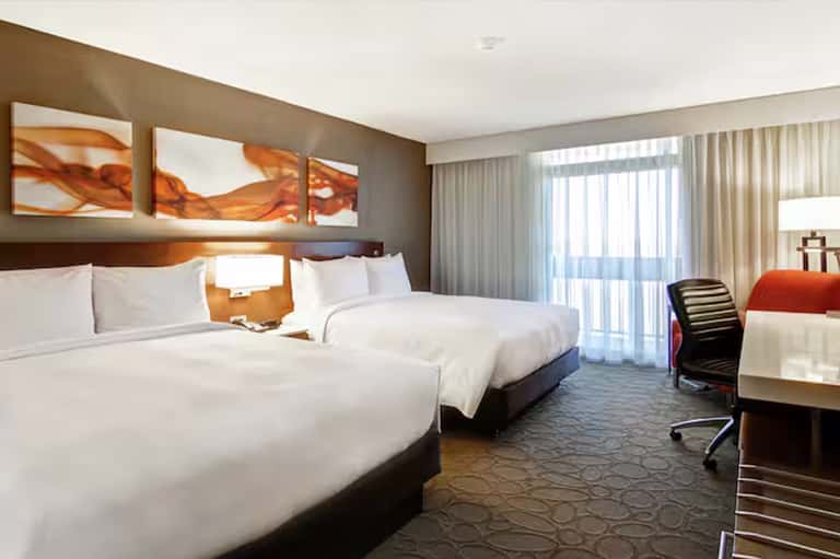 Modern hotel room with two queen beds, orange accents, natural lighting, and work desk