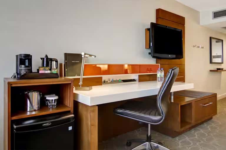 Hotel room workspace with desk, TV, wooden furniture, and orange accent wall
