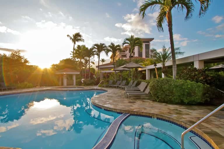 Resort pool at sunset with palm trees, lounge chairs, umbrellas, and landscaped grounds