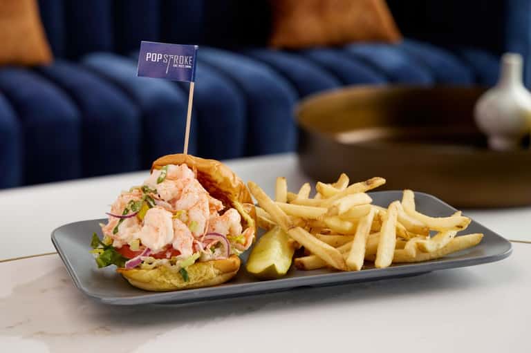 Gourmet shrimp sandwich with fries served at Pop Stroke restaurant with blue velvet seating in background