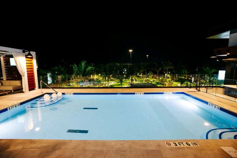 Empty resort swimming pool at night with lit landscaping and palm trees