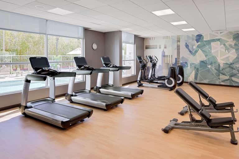 Bright fitness center with treadmills, stationary bikes, and exercise equipment near large windows