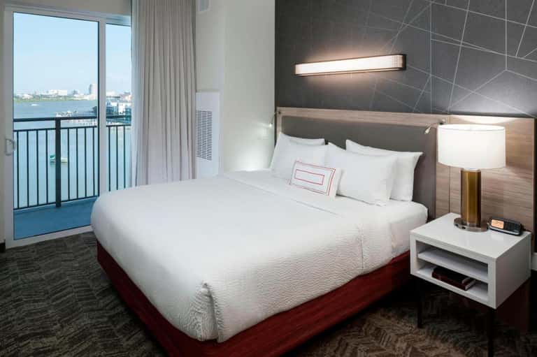 Modern hotel bedroom with waterfront balcony view, contemporary furnishings, and clean white bedding