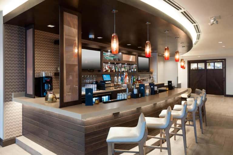 Modern hotel bar with curved counter, pendant lights, wood accents, and bar seating