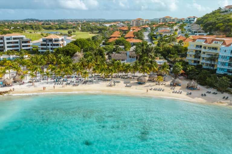 Aerial view of beach resort with turquoise water, palm trees, and beachfront buildings