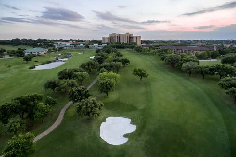 Aerial view of resort on golf course with fairway bunker, trees, pond, and main building in distance