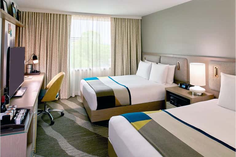 Hotel room with two queen beds, blue and yellow accents, work desk, and floor-to-ceiling curtains