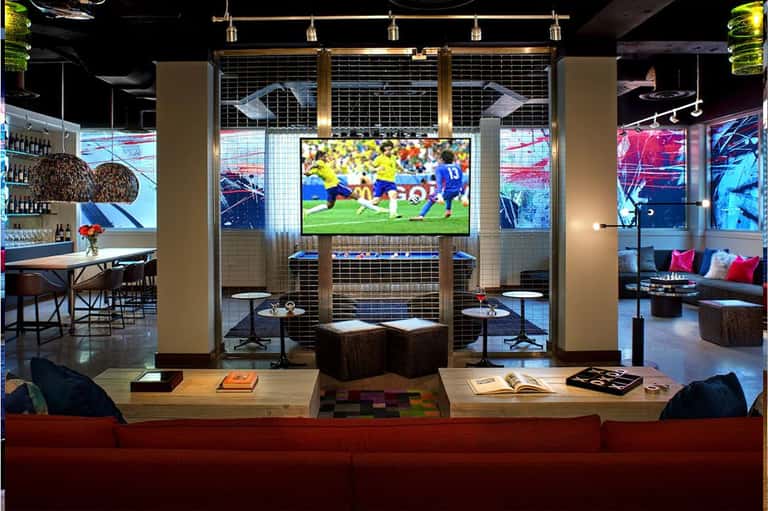 Sports bar lounge with large TV screen showing soccer match, red sofa, and modern lighting