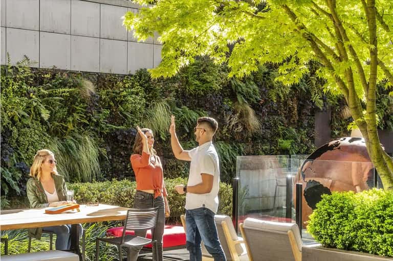 Outdoor patio with guests socializing among lush green vegetation and modern architecture