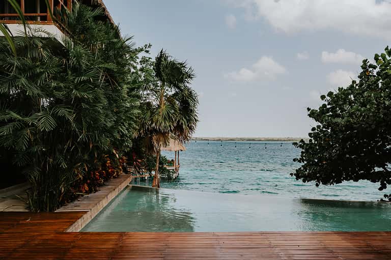 Wooden deck extending into turquoise ocean water surrounded by tropical vegetation and palm trees