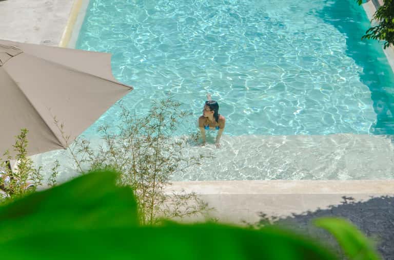 Woman swimming in indoor resort pool with turquoise water, white loungers, and sandy beach area