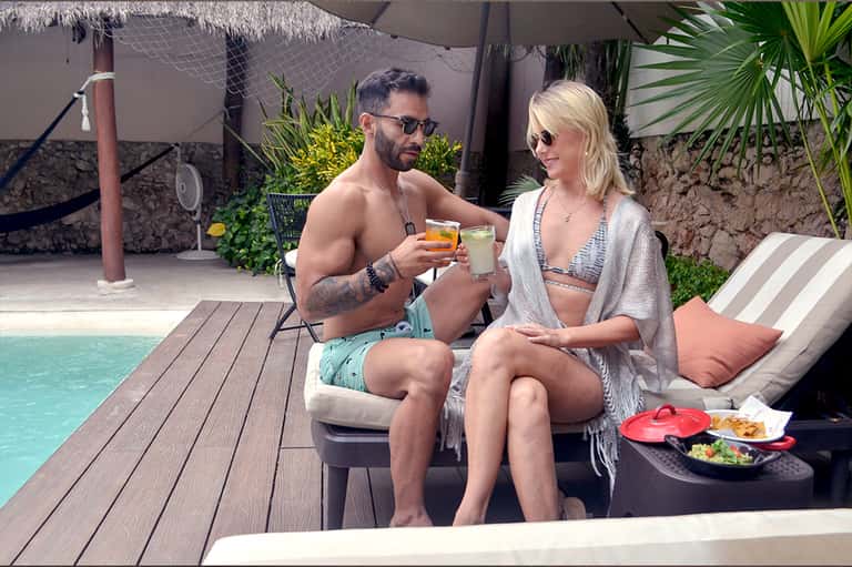 Couple enjoying drinks poolside at tropical resort with thatched roof and beach access