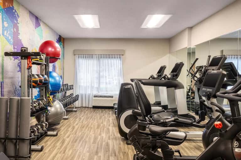 Modern fitness center with exercise equipment, colorful accent wall art, and mirrored walls