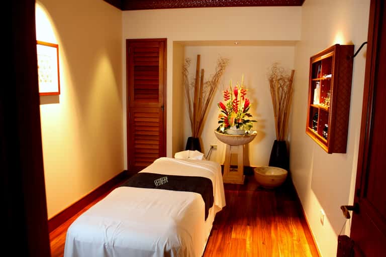 Spa massage room with white massage table, wooden accents, red decorative elements, and warm lighting