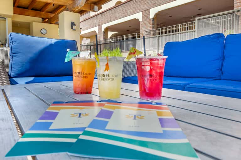 Poolside lounge area with blue cushioned seating, colorful geometric pattern, and tropical cocktails