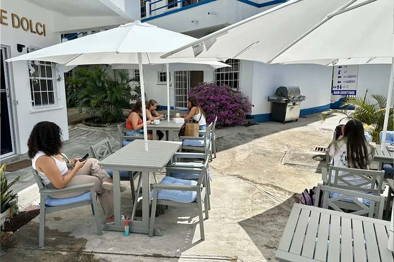 Outdoor beachside dining area with white umbrellas, purple bougainvillea flowers, and casual seating