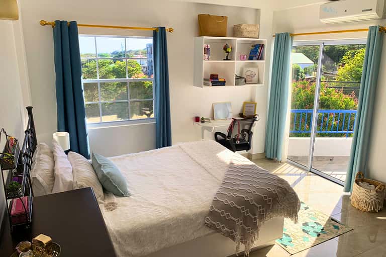 Bright hotel bedroom with queen bed, turquoise curtains, balcony doors, and scenic views