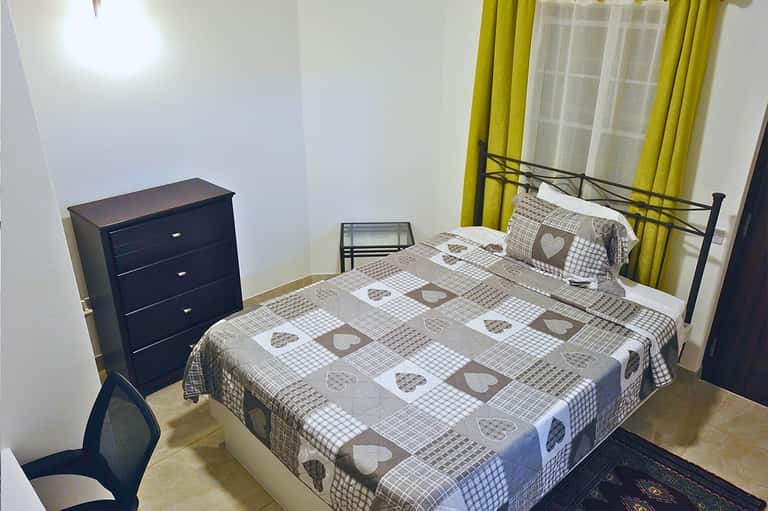 Simple bedroom with double bed, dark dresser, green curtains, and basic furnishings